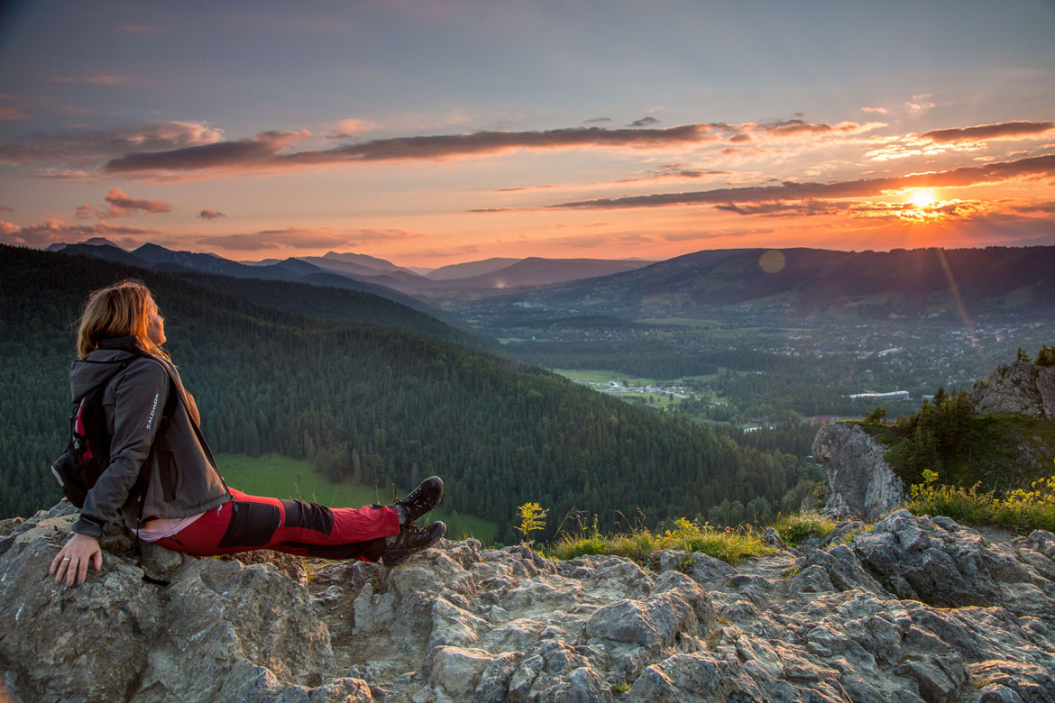 woman sitting on top of a cliff watching sunset